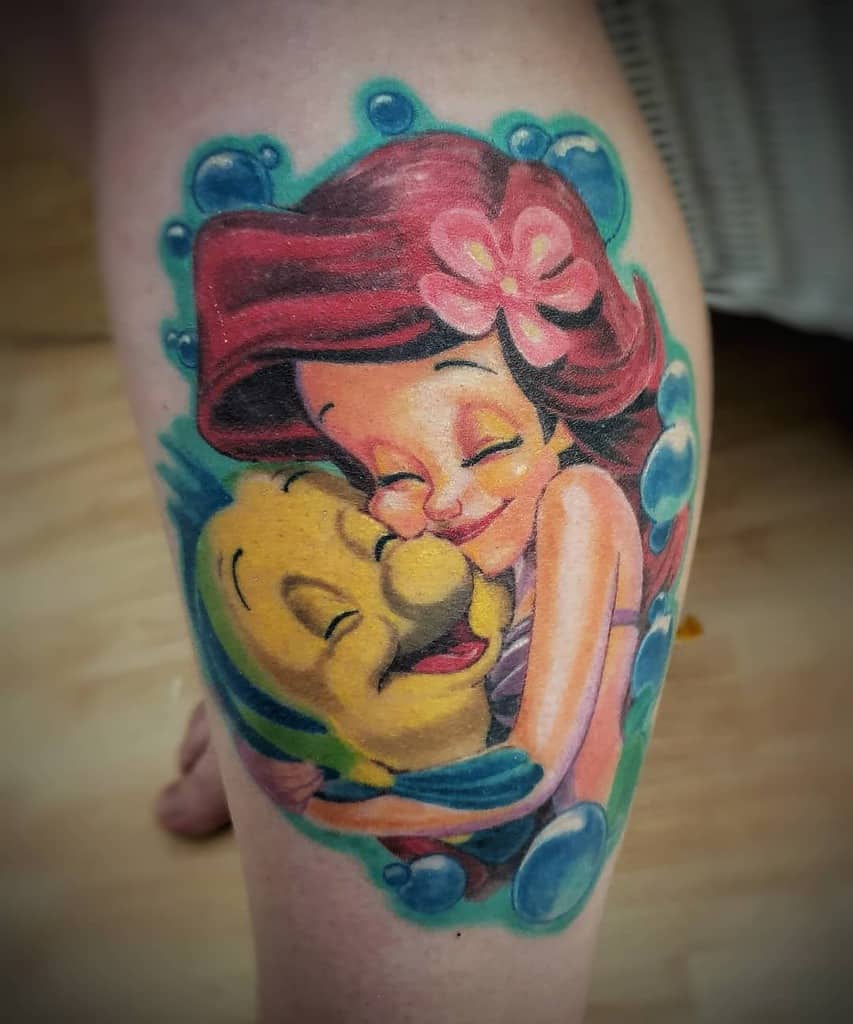 Heartwarming Ariel tattoo hugging Flounder, featuring vibrant colors, playful bubbles, and a flower in her hair for a cheerful design