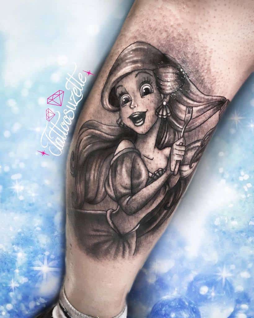 Elegant black-and-gray Ariel tattoo with flowing hair, a joyful expression, and her iconic fork, showcasing intricate shading on the leg