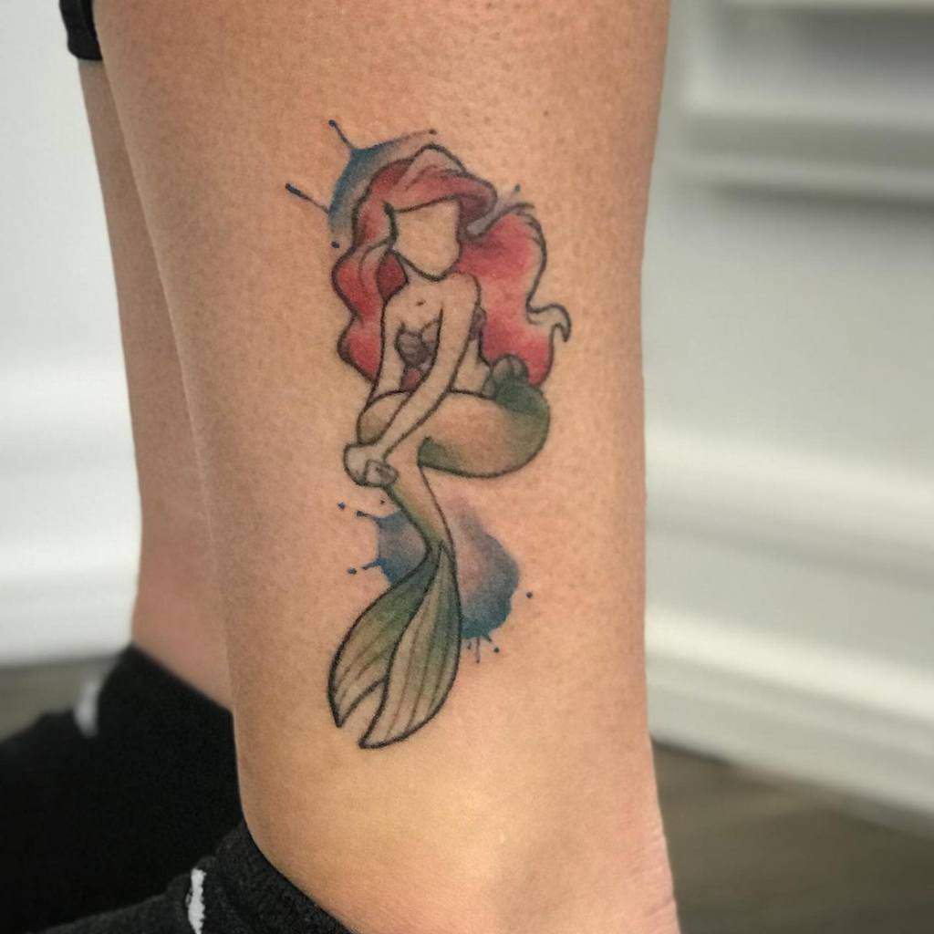 Artistic Ariel tattoo with a faceless design, flowing red hair, and a watercolor background, creating a minimal yet creative look
