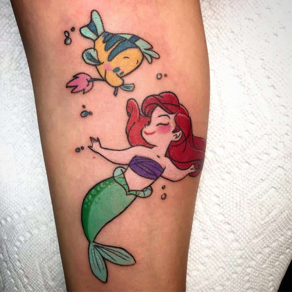 Adorable Ariel and Flounder tattoo with playful expressions, vibrant colors, and bubbles, showcasing a fun underwater scene