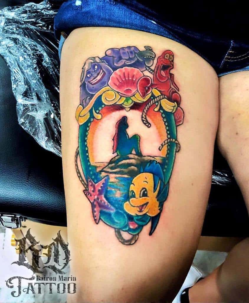 Vibrant Little Mermaid tattoo featuring Ariel's iconic silhouette, Flounder, Sebastian, Ursula, and ocean-themed details in a bold thigh design