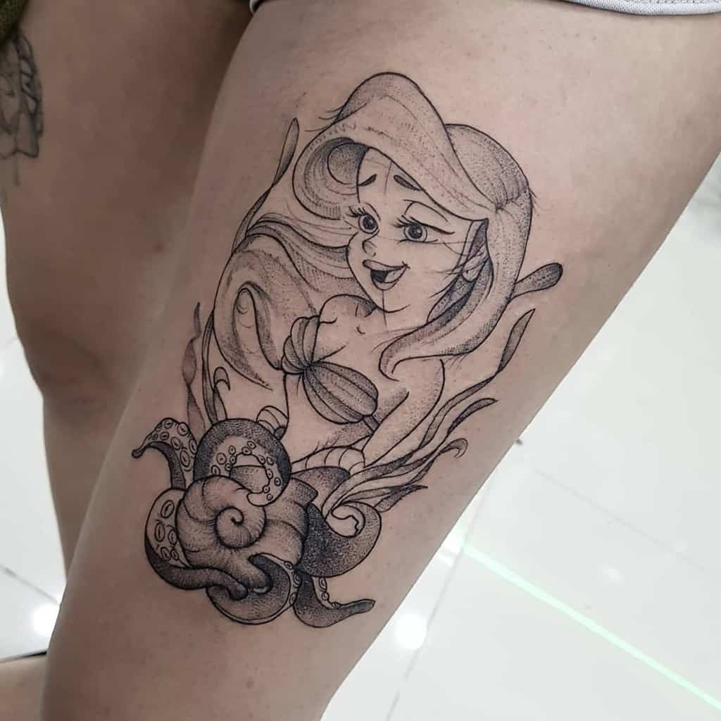 Detailed black-and-gray Ariel tattoo with flowing hair, expressive features, and intricate seashell and tentacle elements on the thigh