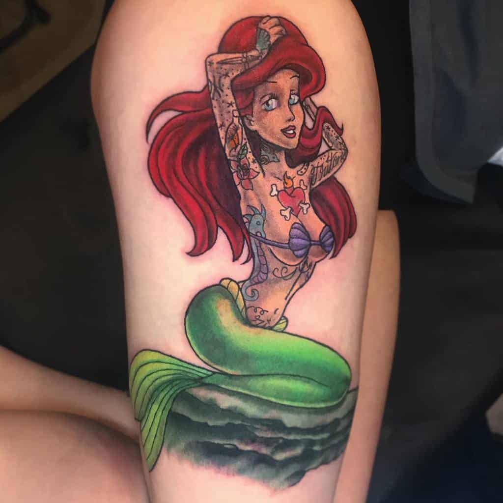 Bold thigh tattoo of Ariel with a modern twist, featuring intricate tattoo designs on her arms and torso, blending classic Disney with contemporary art