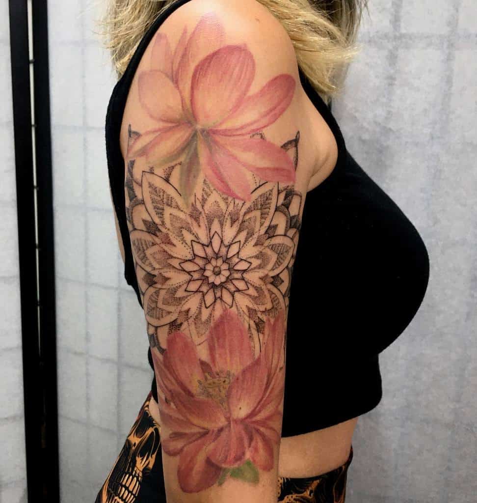 Arm with a detailed floral tattoo featuring large pink flowers and intricate mandala designs
