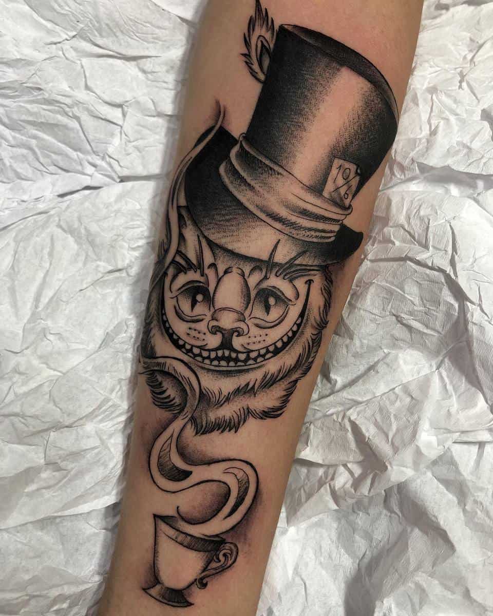 Cheshire Cat tattoo with a Mad Hatter hat and teacup, capturing Wonderland’s whimsical essence