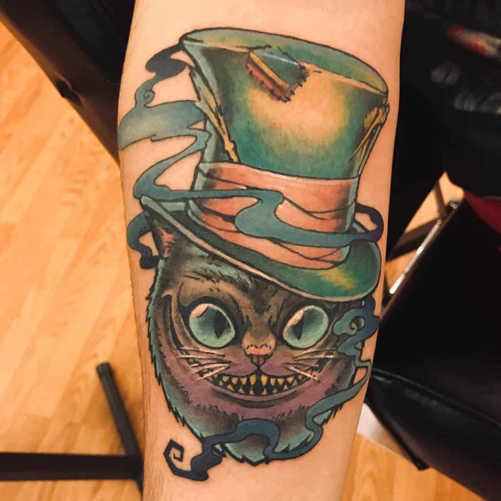 Cheshire Cat tattoo with a colorful Mad Hatter hat and swirling smoke details