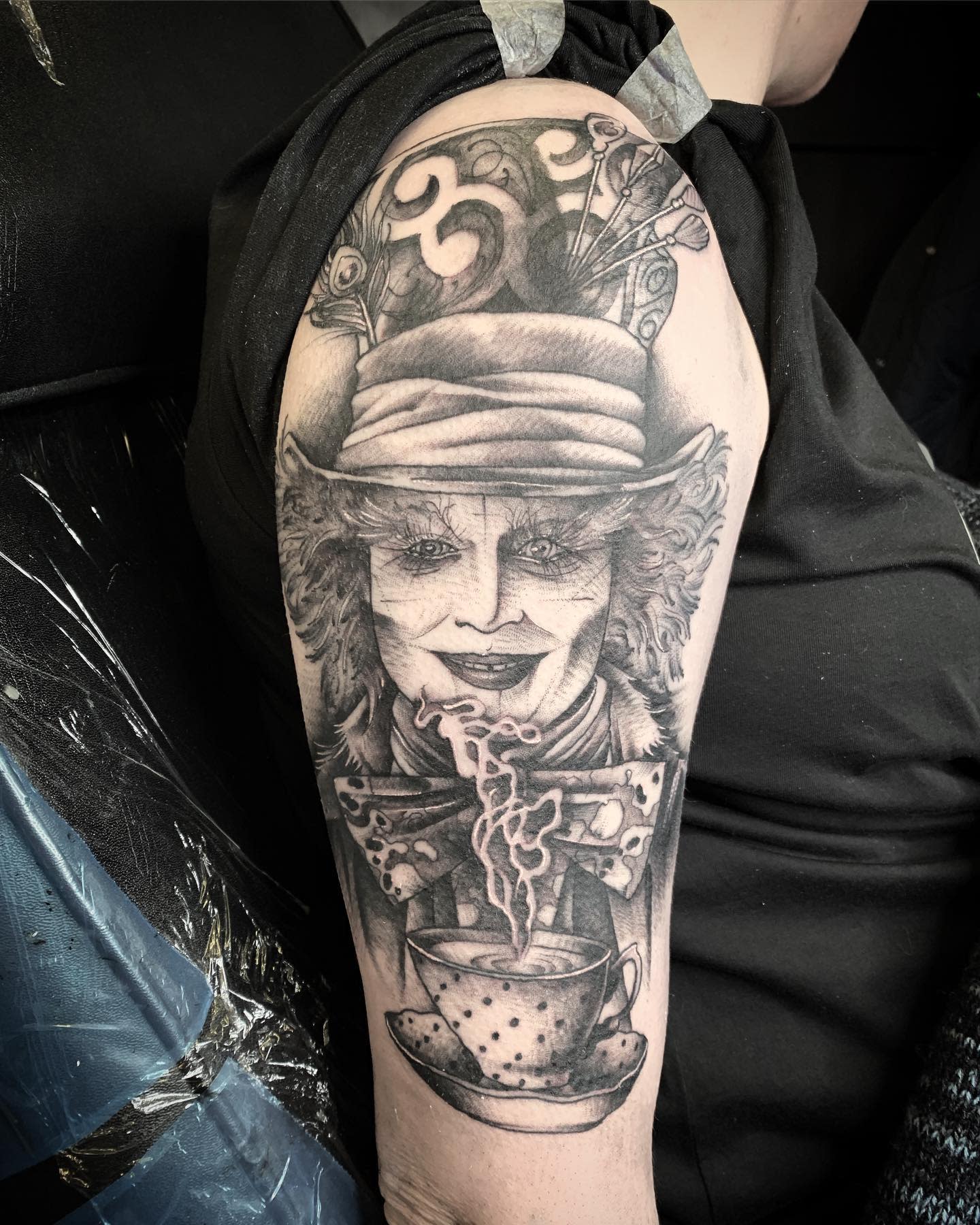 Detailed black and grey tattoo of the Mad Hatter with a steaming teacup, symbolizing his eccentricity