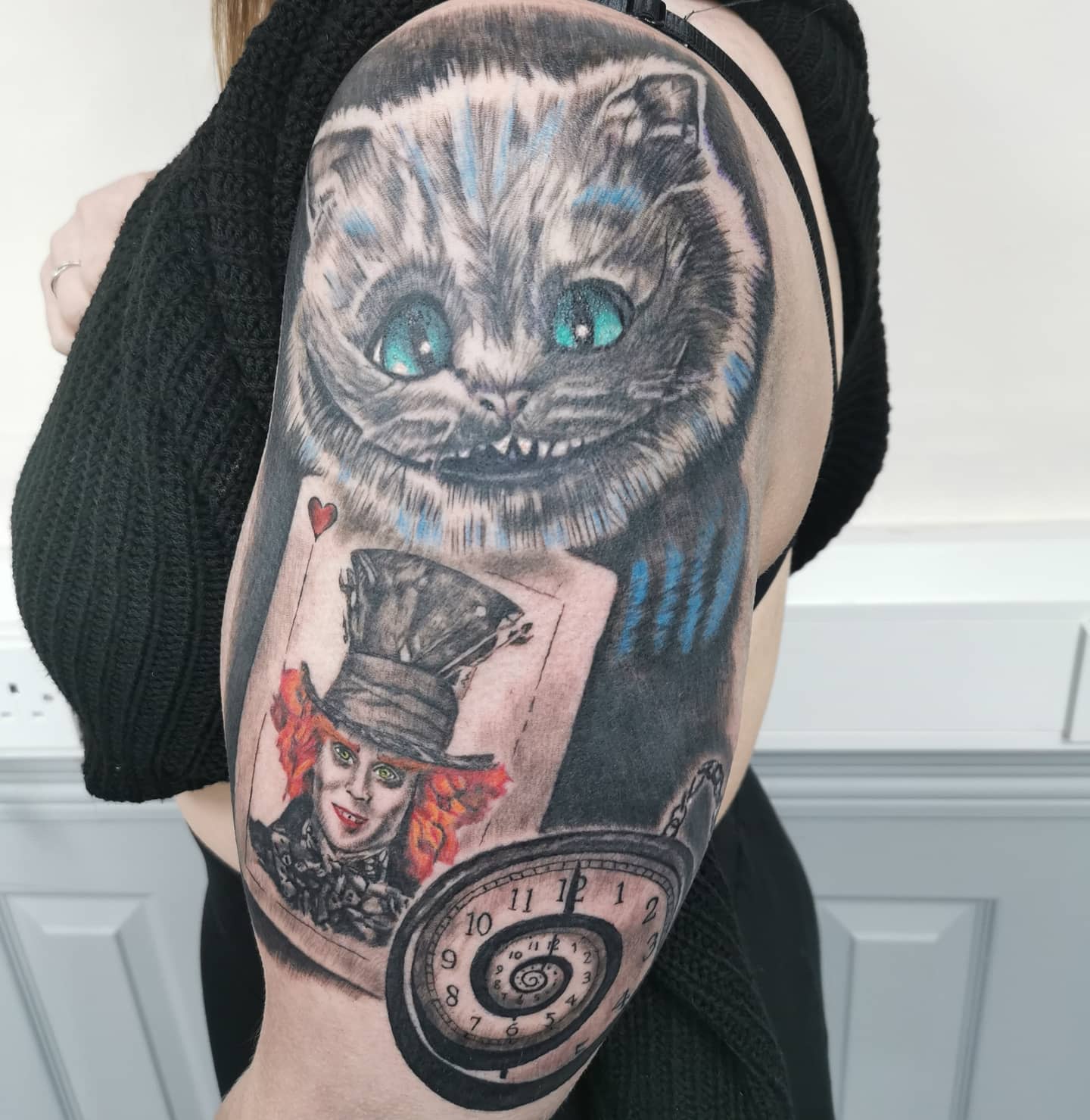 Detailed tattoo featuring the Cheshire Cat, a playing card with the Mad Hatter, and a spiral clock
