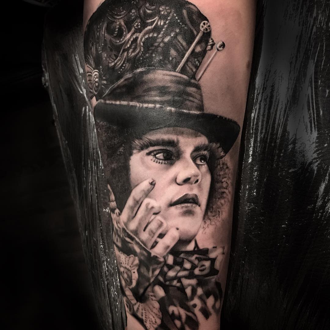 Realistic black and grey tattoo of the Mad Hatter with a focused expression, detailed hat, and intricate lace