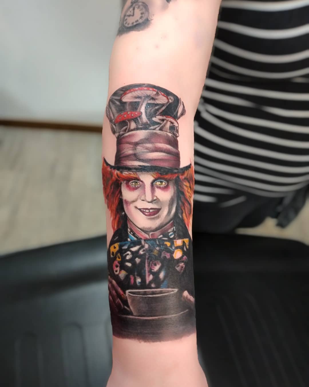Realistic tattoo of the Mad Hatter holding a teacup, with vibrant colors highlighting his signature hat and eccentric expression