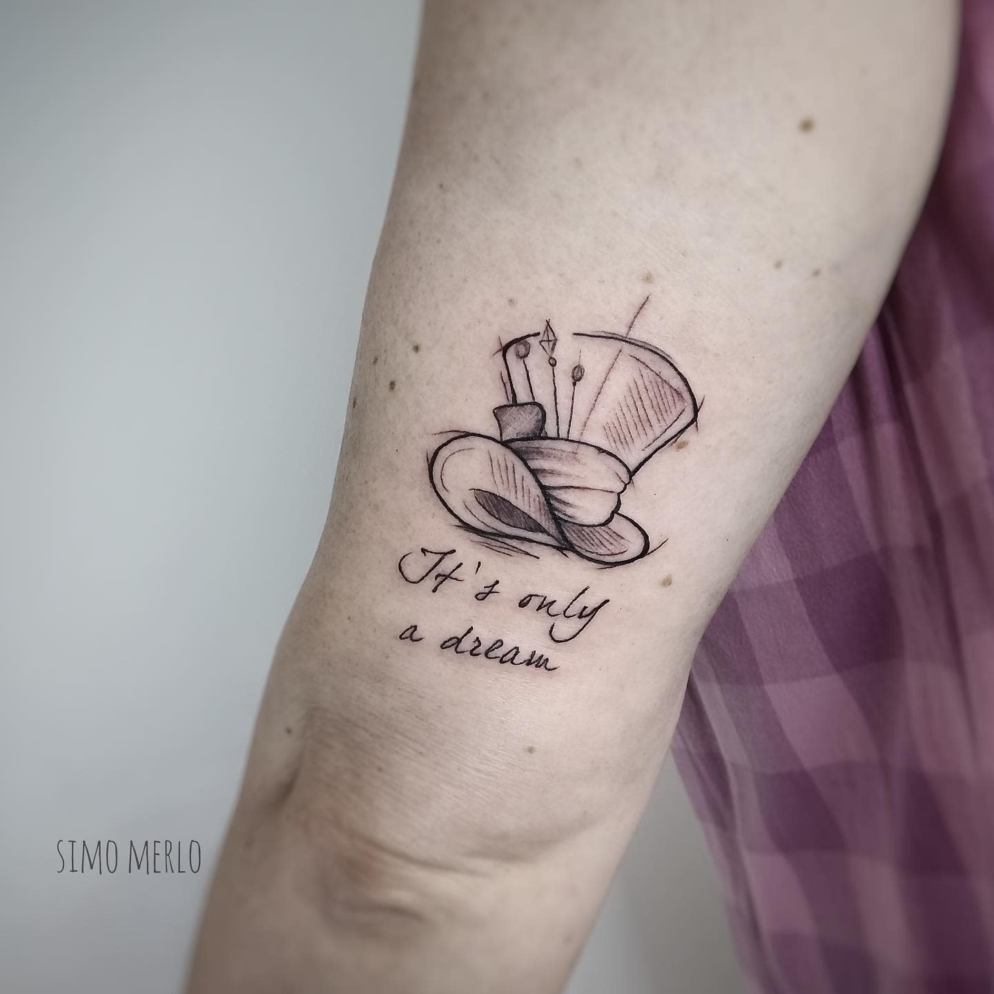 Simple tattoo of the Mad Hatter’s hat with the phrase 'It’s only a dream,' reflecting the surreal nature of Wonderland