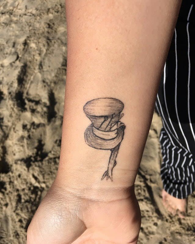 Minimalist wrist tattoo of the Mad Hatter’s hat with delicate linework, symbolizing Wonderland’s whimsy
