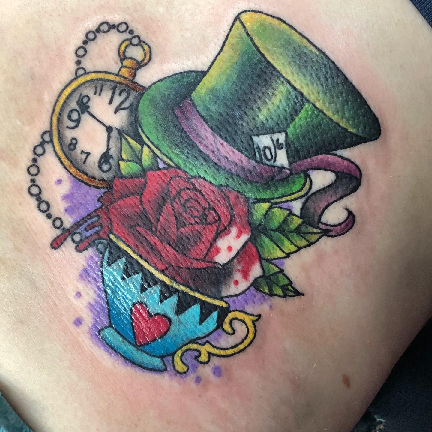 Colorful tattoo of the Mad Hatter’s hat, pocket watch, rose, and teacup, symbolizing Wonderland’s whimsy