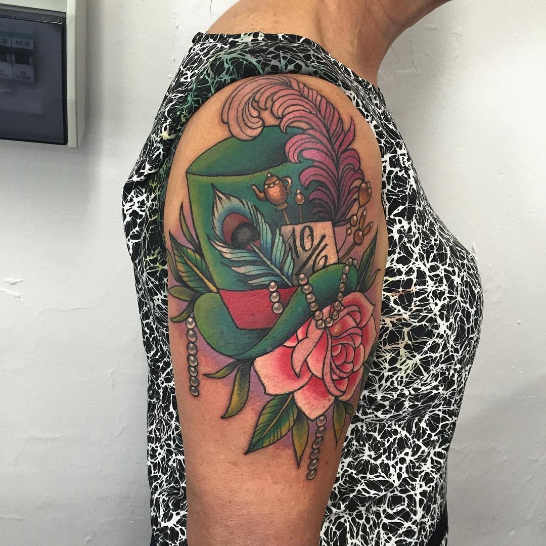 Bold tattoo of the Mad Hatter’s hat with a teacup, feather, and rose, adorned with pearls and vibrant colors