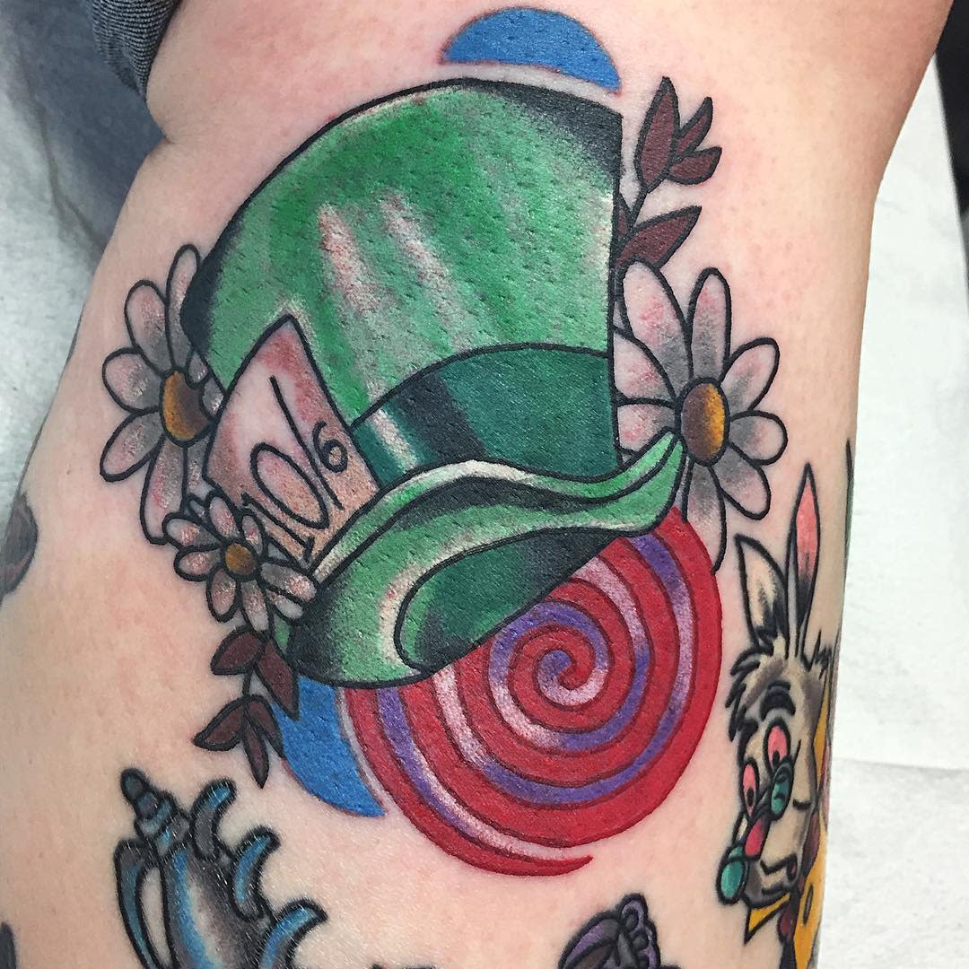 Traditional tattoo of the Mad Hatter’s green hat with daisies and a red and blue spiral background