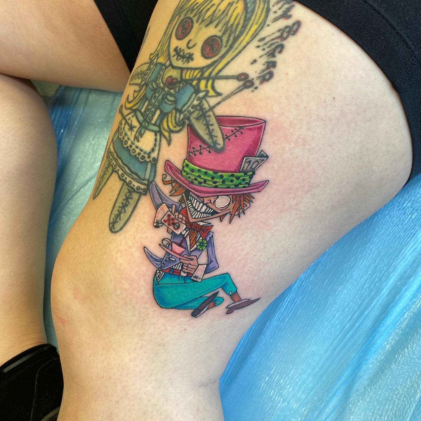 Whimsical tattoo of a stylized Mad Hatter with vibrant colors and exaggerated features, holding a teacup