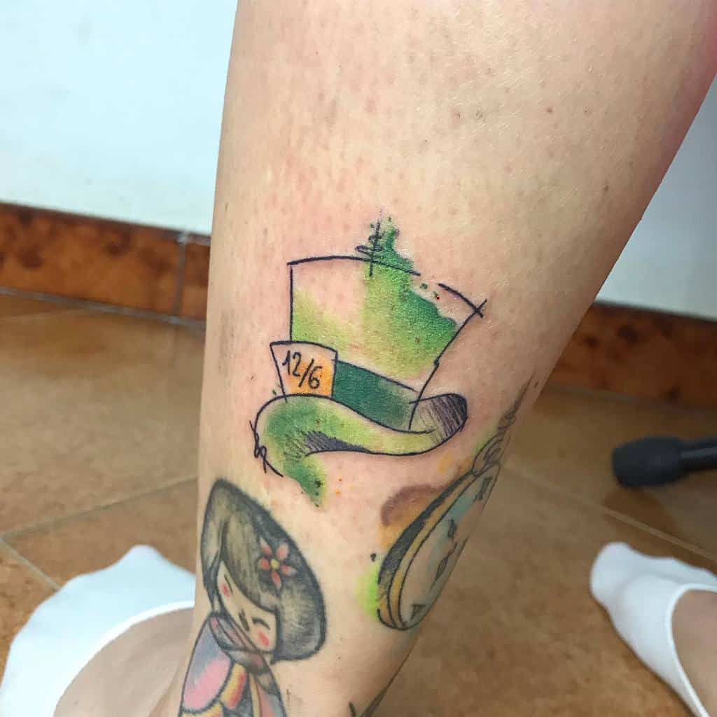 Colorful tattoo of the Mad Hatter’s hat from Alice in Wonderland, with the price tag reading '12/6' and watercolor-style splashes of green around it