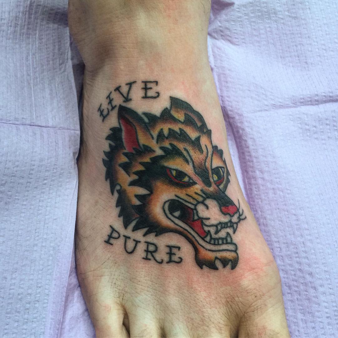 Tattoo on a foot featuring a fierce wolf's head with the words "LIVE PURE" in uppercase letters above and below