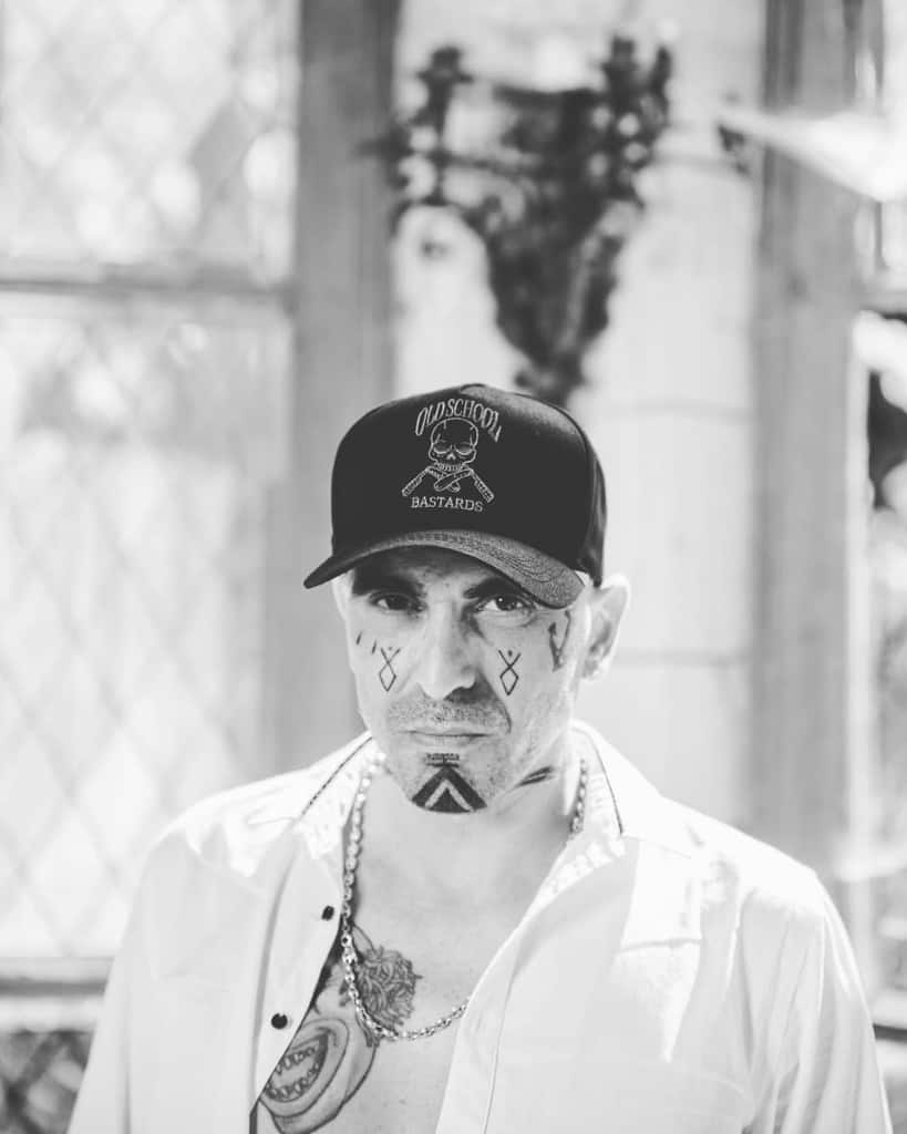 A man with minimalist tribal face tattoos, including geometric symbols under his eyes and on his chin