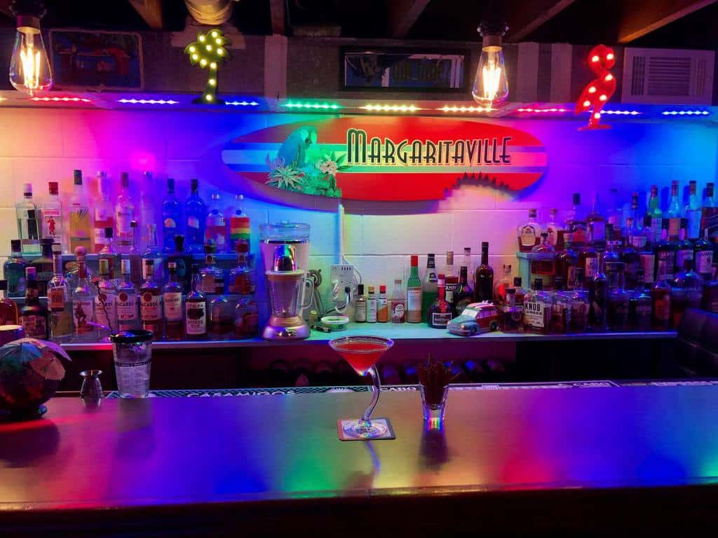 Margaritaville-themed man cave cocktail bar with colorful LED lighting and various liquors displayed.