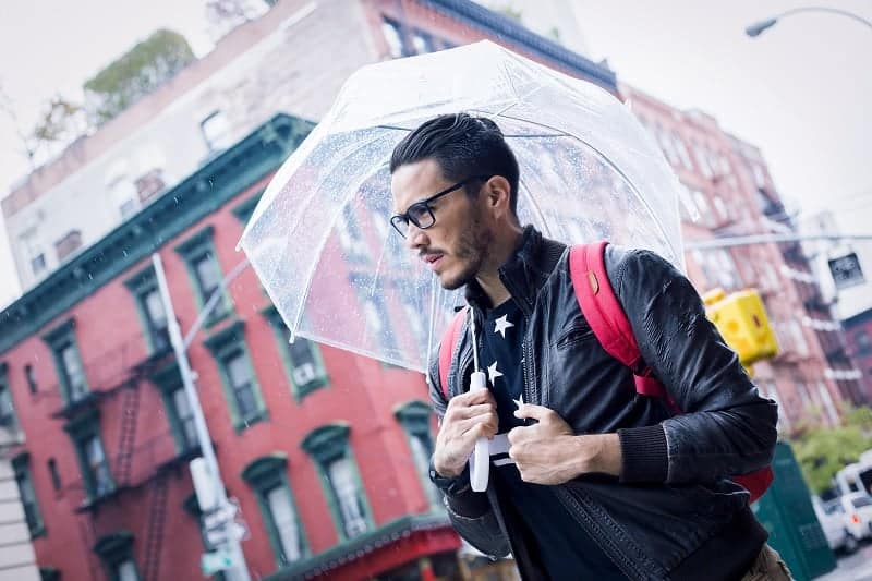 Fashionable man with umbrella walking down street in rain