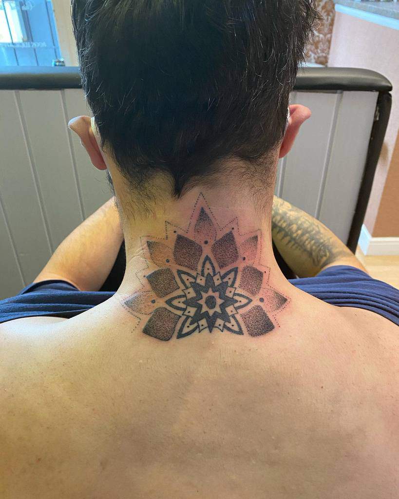 Back view of a person with a geometric star tattoo on the back of their neck, sitting in a chair