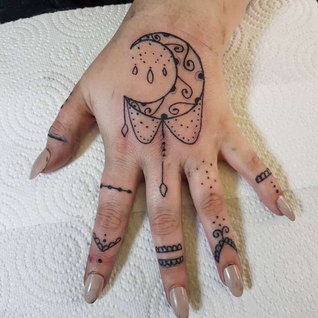 Hand tattoo with a crescent moon, intricate patterns, and dotted fingers