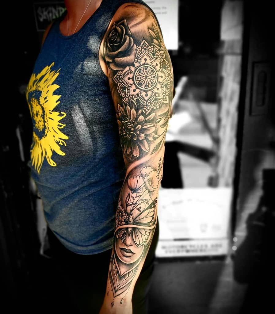 A stunning sleeve tattoo featuring a rose, intricate mandala, vibrant flowers, and a mysterious woman with her eyes elegantly covered by a butterfly