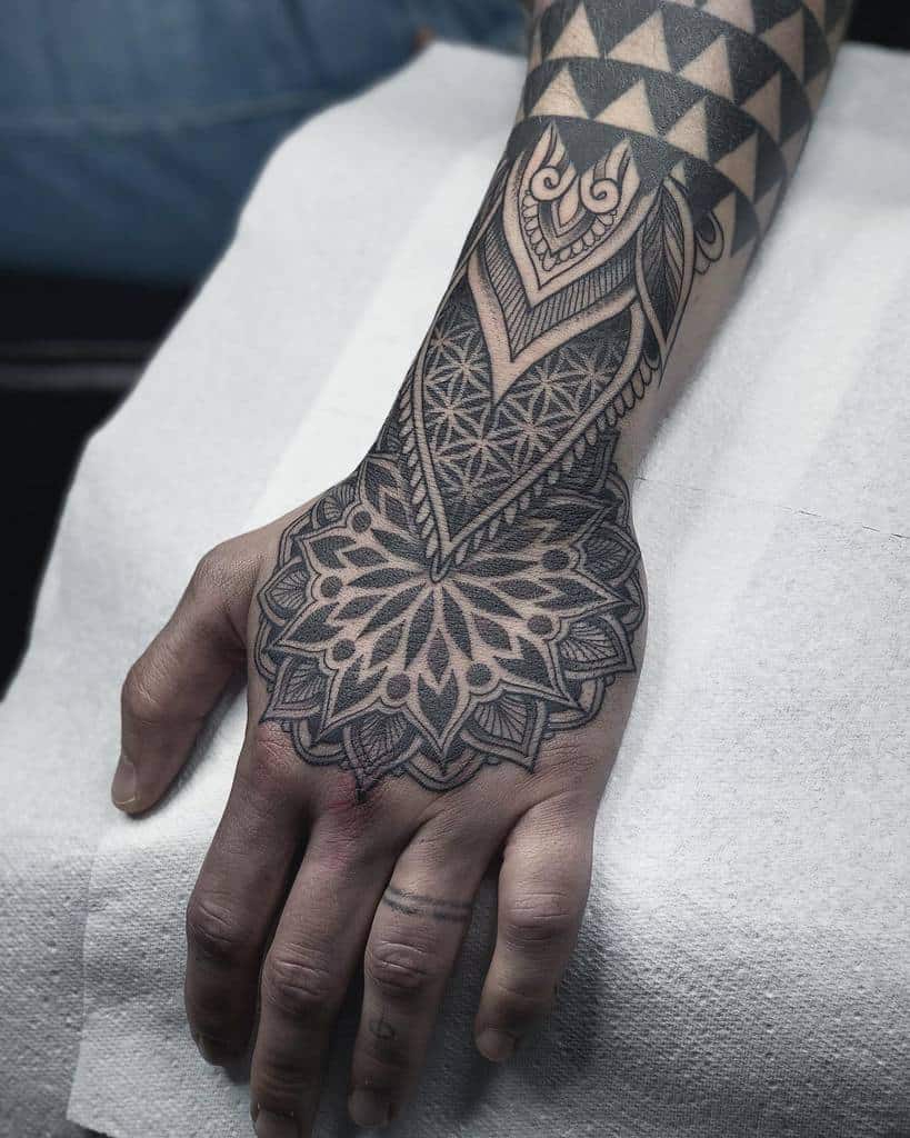 A hand with intricate geometric and floral black ink tattoos 