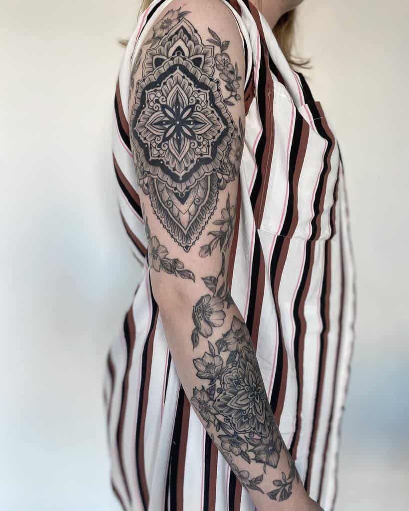 This mandala-inspired sleeve tattoo features intricate geometric patterns beautifully paired with delicate floral accents, creating a harmonious and elegant design that flows seamlessly along the arm