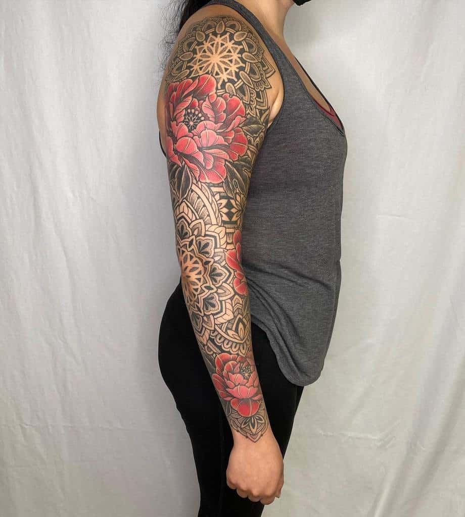A full sleeve tattoo featuring intricate mandala patterns in black and grey, with vibrant red peony flowers, extending from the shoulder to the wrist, blending geometric and floral elements