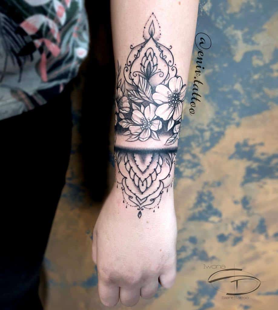 Ornate forearm tattoo with mandala and floral design, including leaves and detailed shading