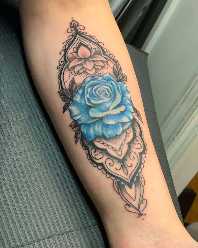 Tattoo of a blue rose with an intricate black mandala design on a forearm