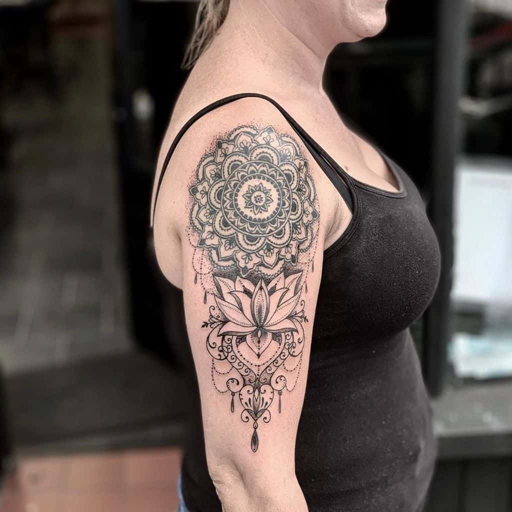 Elegant black and grey lace tattoo on upper arm featuring a mandala, lotus flower, and ornamental details with fine line shading.
