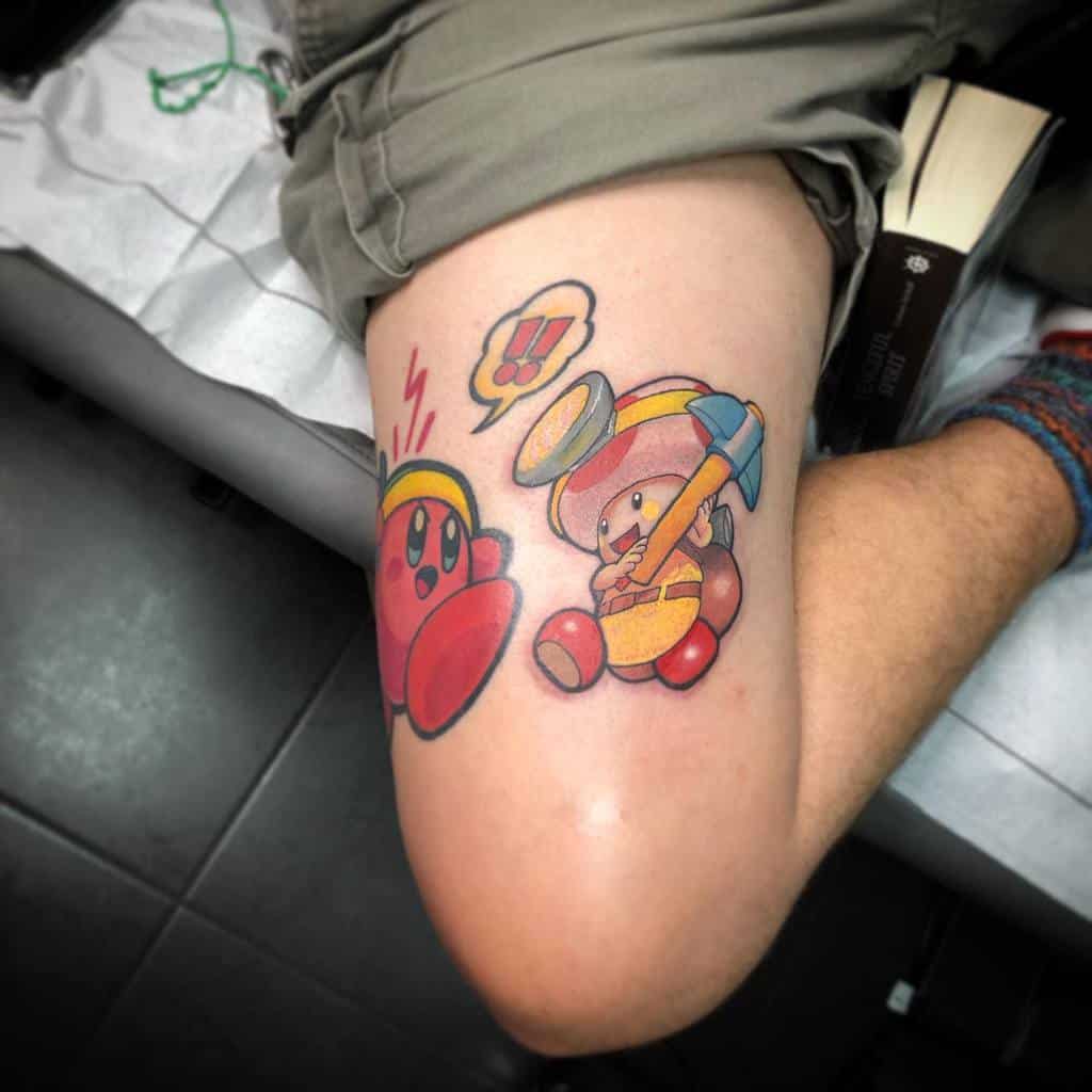 Tattoo of Kirby and Toad from Super Mario, both wearing helmets and holding hammers, Kirby looks shocked as Toad raises his hammer