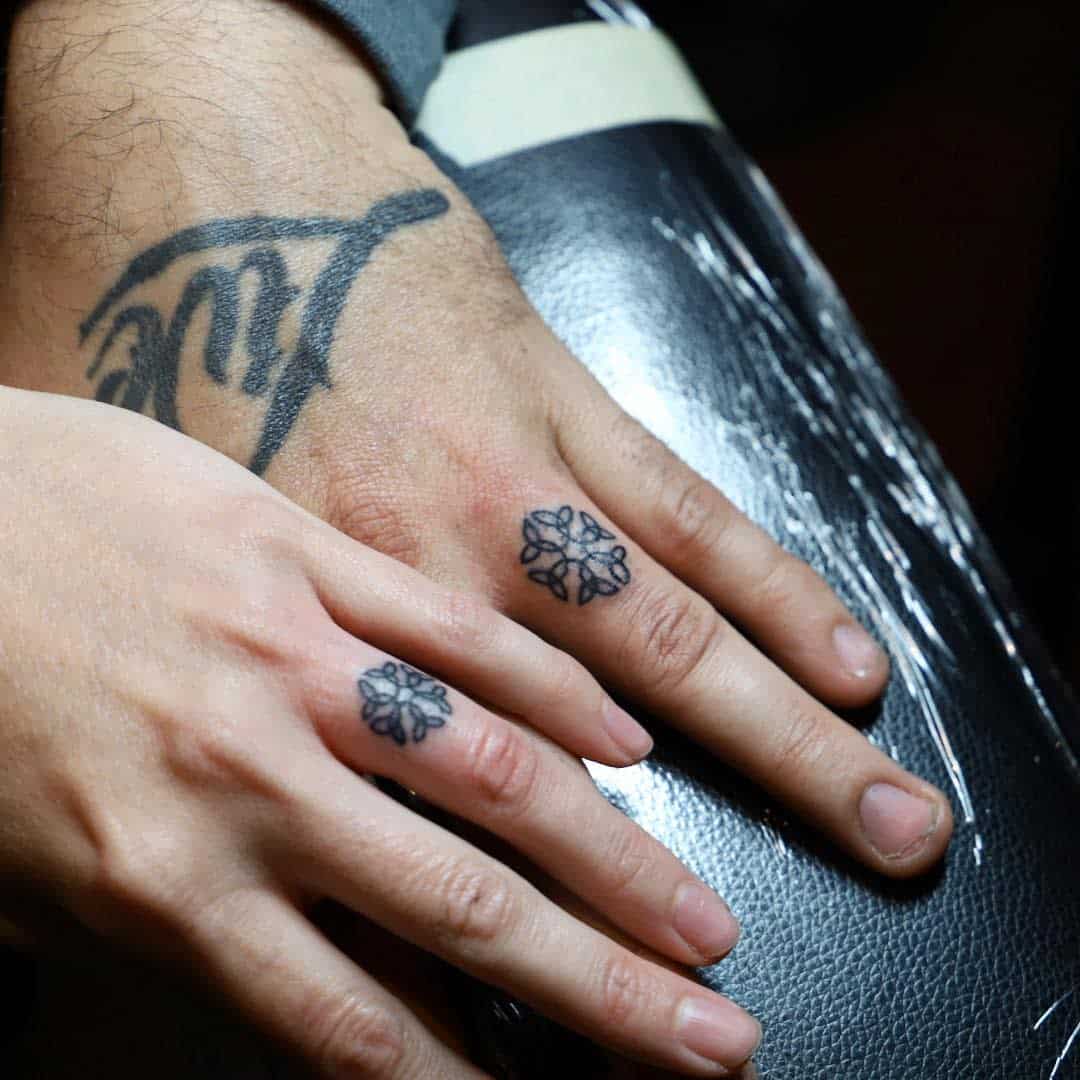 Two hands with matching geometric tattoos on the fingers, placed side by side