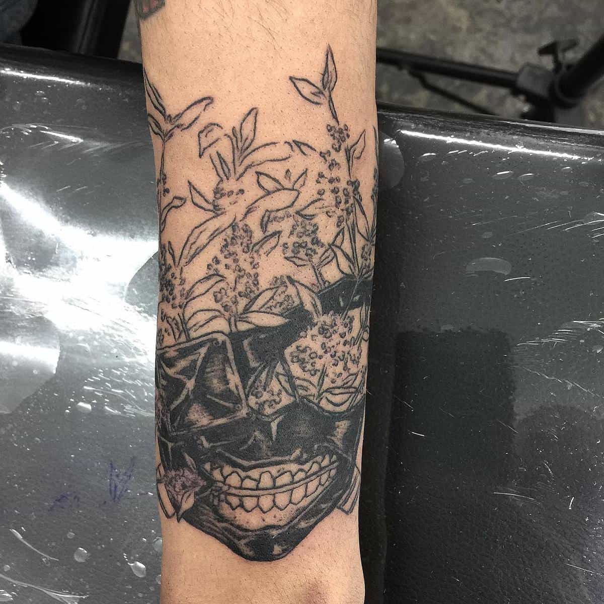 Forearm tattoo of Kaneki Ken's ghoul mask from Tokyo Ghoul, intertwined with delicate flowers and leaves.