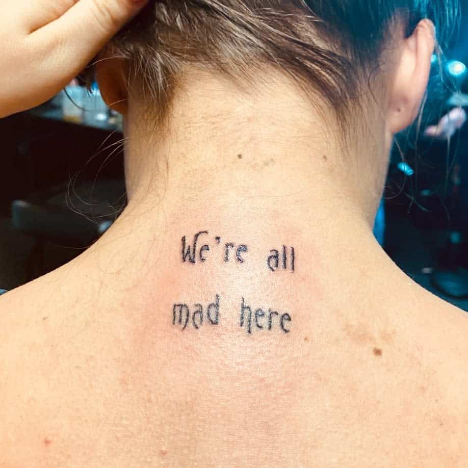 Tattoo on the back of neck reads "We're all mad here" in black ink