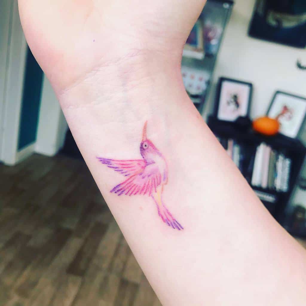 Tattoo of a pink and purple hummingbird gracefully perched on the back of the neck