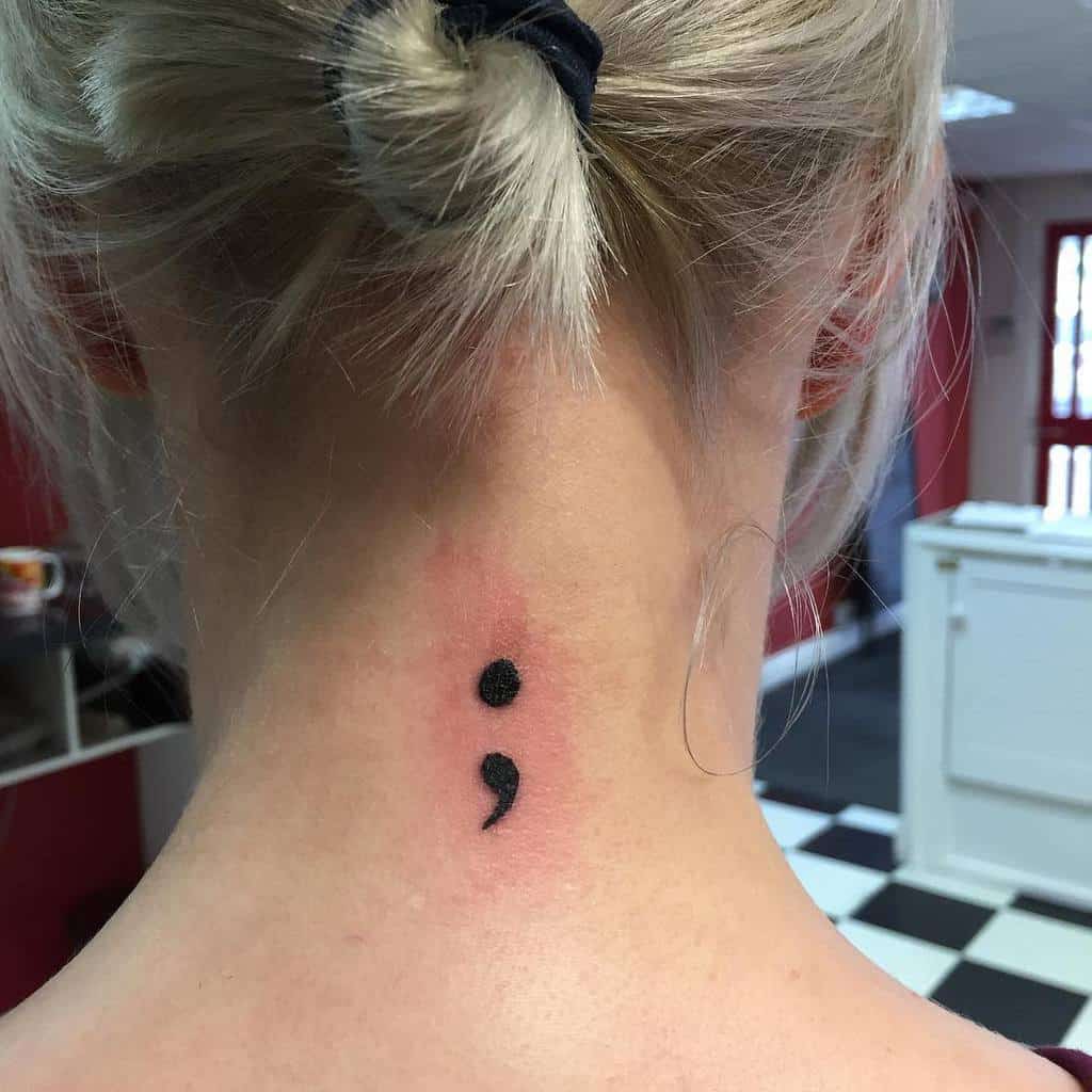 A semicolon tattoo elegantly placed just below the hairline on the back of the neck