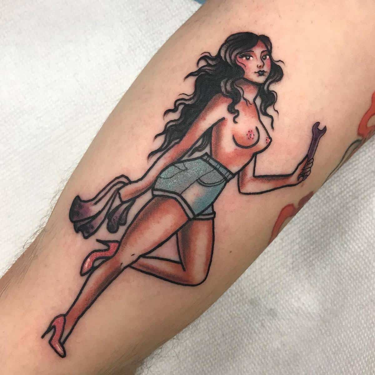 Tattoo of a woman with long hair and shorts, holding a wrench and cloth, on an arm