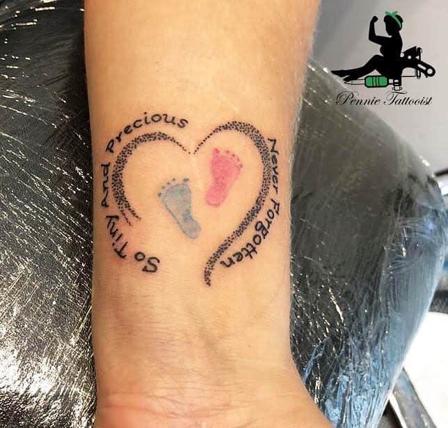 Tattoo of two baby footprints inside a heart with the text "Never forgotten" and "So tiny and so Precious"