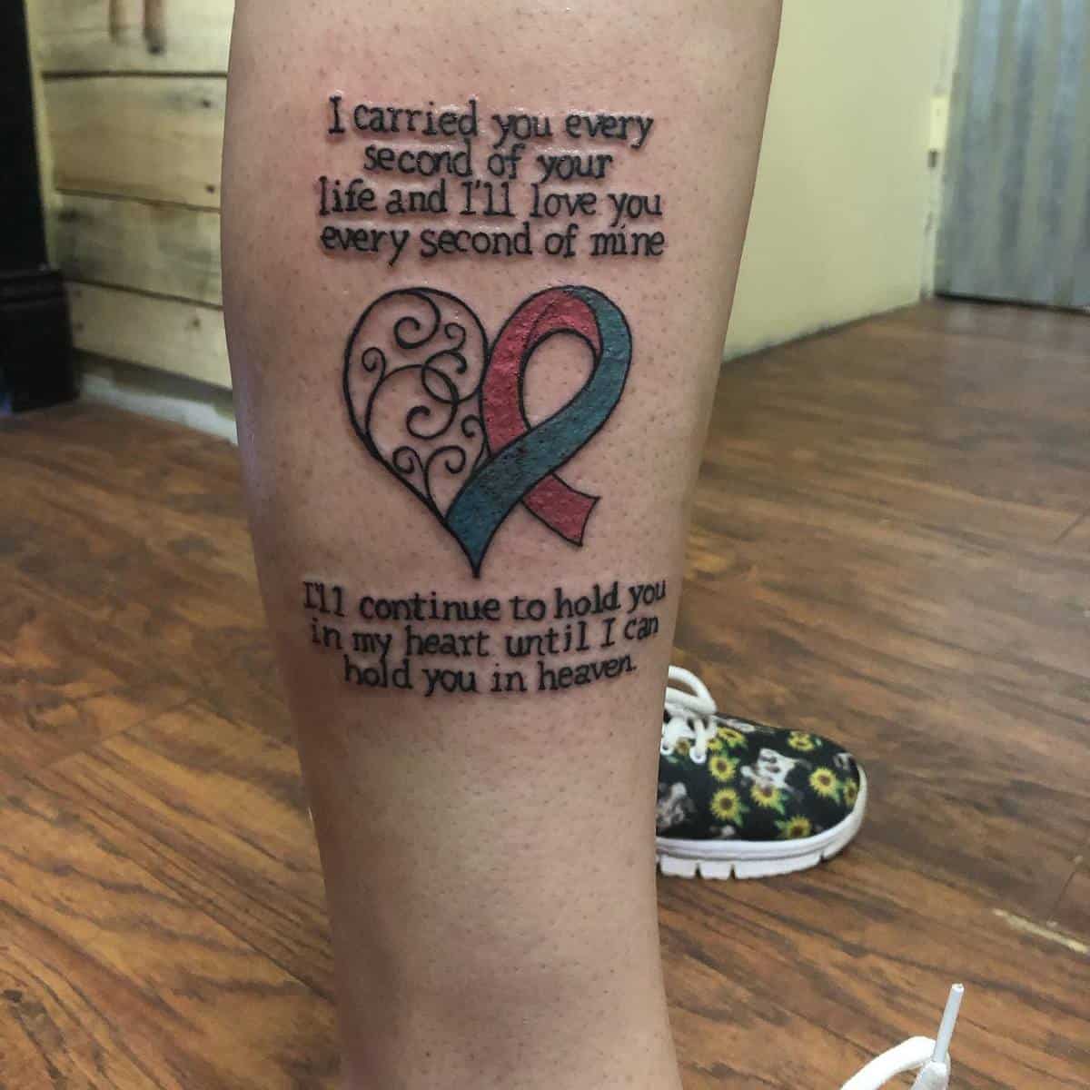 A tattoo featuring a heart symbol, a ribbon, and a memorial quote on the back of a calf