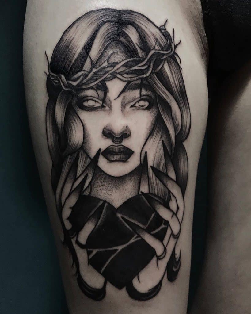 Tattoo of a woman with long hair, wearing a thorn crown, holding a cracked black heart with long nails in black and gray shading