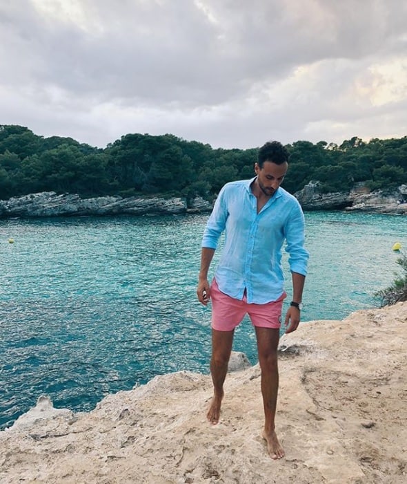 Man wearing button-down blue shirt and pink shorts near sea