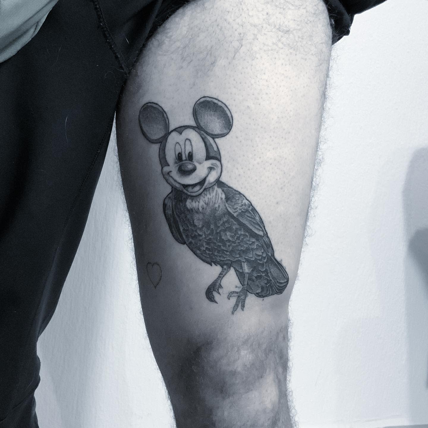 Black-and-gray tattoo of a bird with Mickey Mouse's head replacing the bird's head