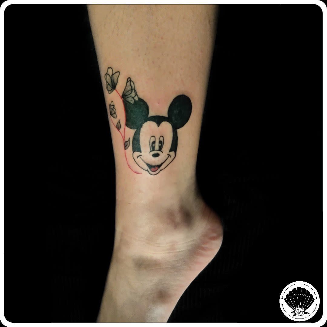 Tattoo of Mickey Mouse's face on an ankle, with a vine of roses wrapping around one ear