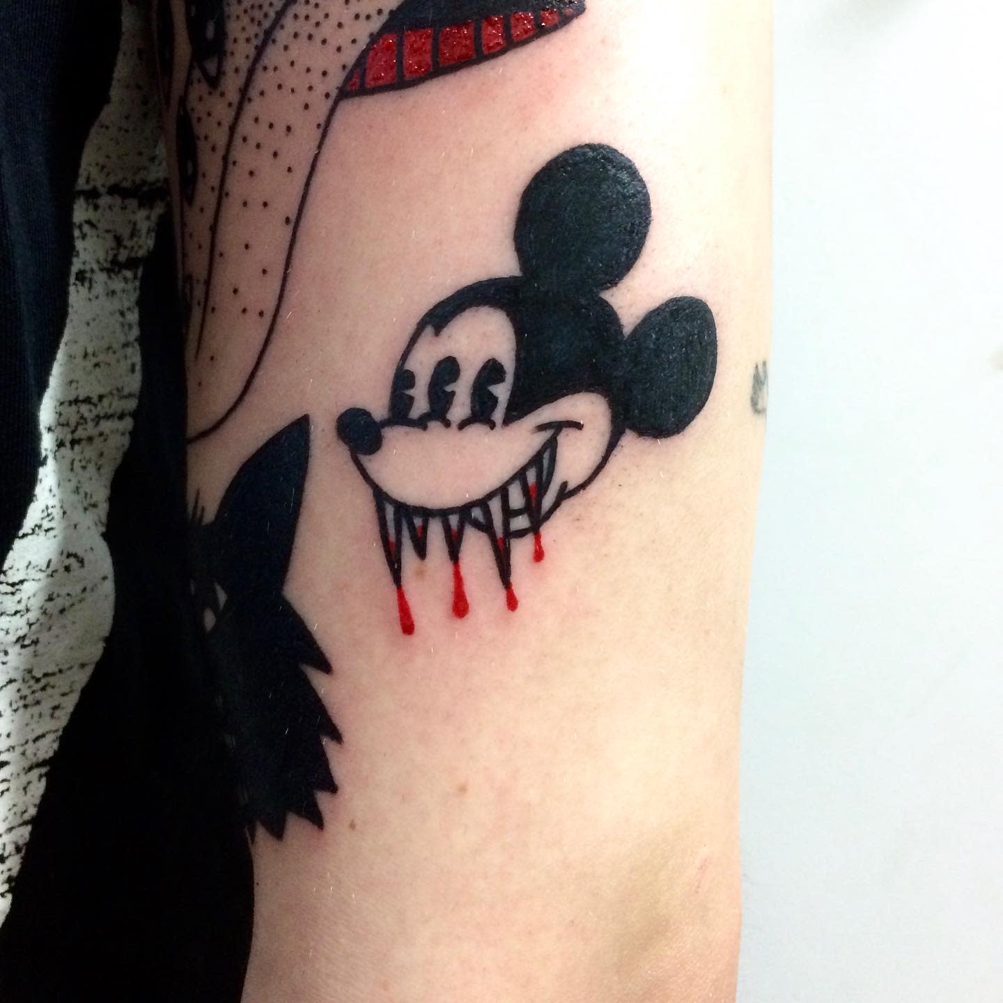 Tattoo of a sinister-looking Mickey Mouse with sharp fangs dripping red blood