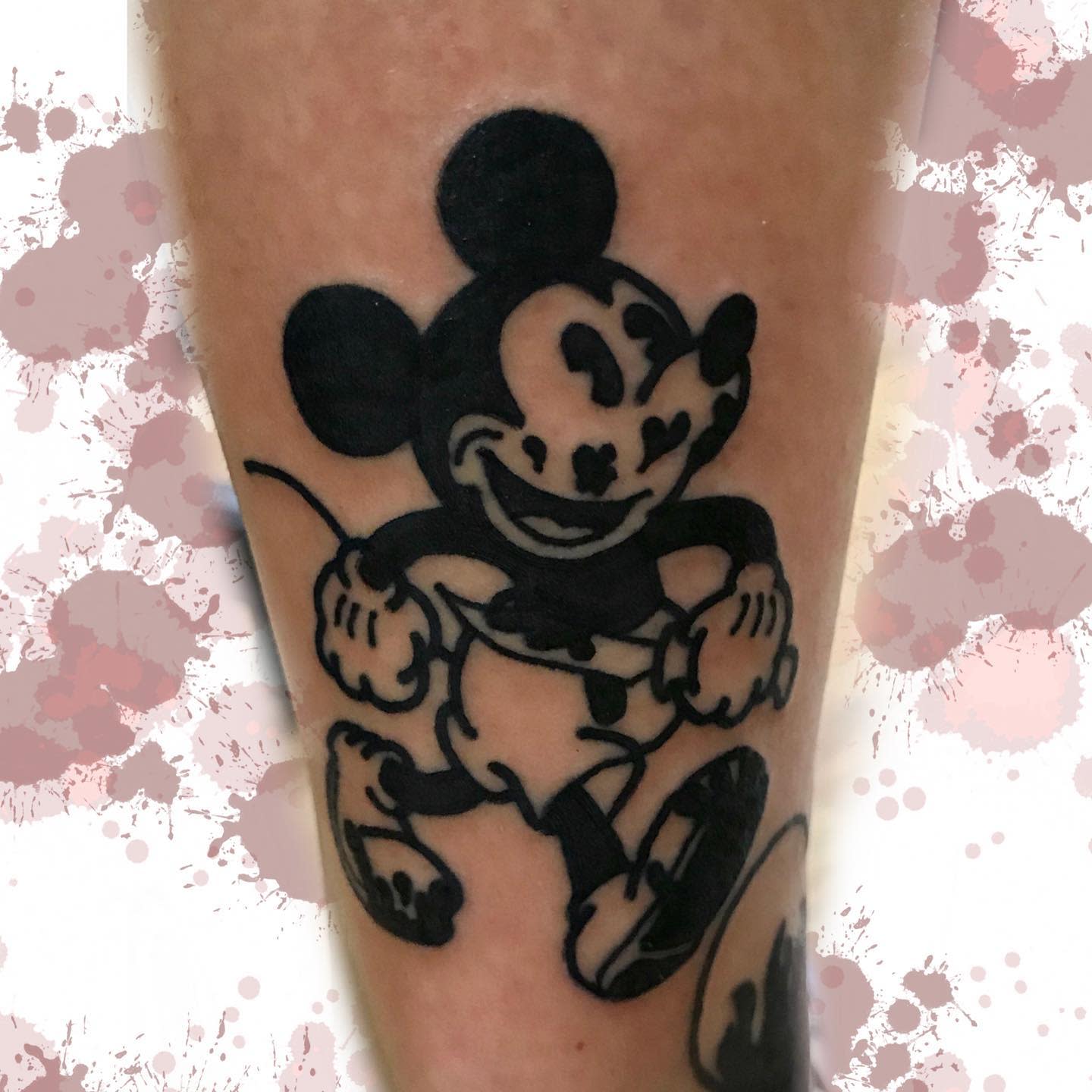Bold black-and-gray tattoo of a distorted, mischievous Mickey Mouse holding a rope, placed on a leg
