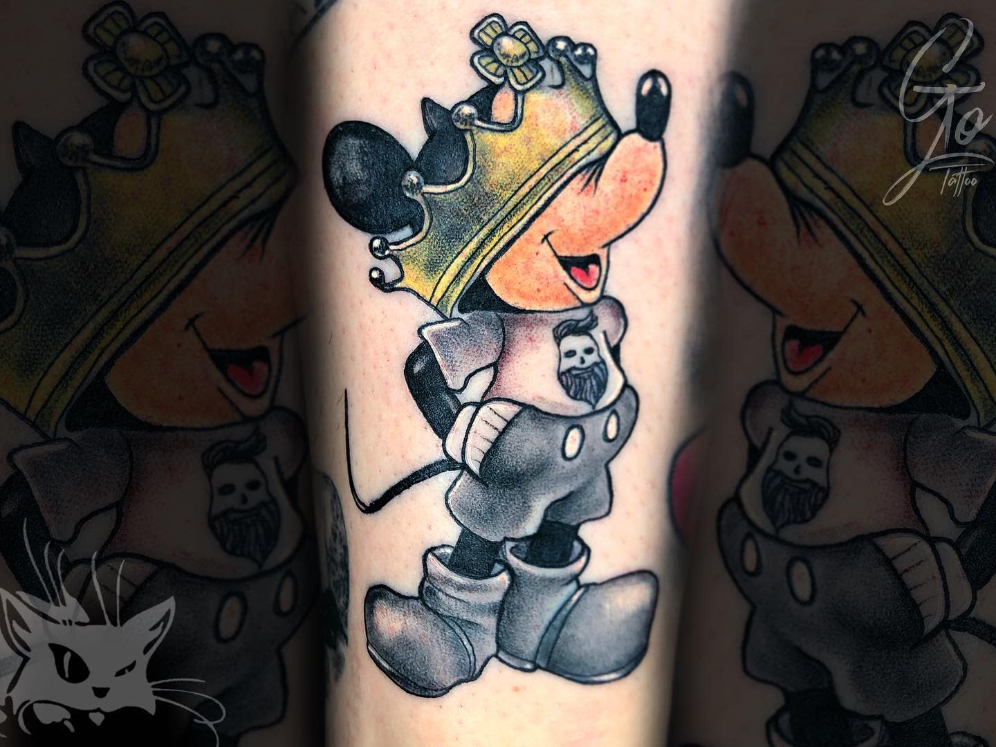 Colorful tattoo of Mickey Mouse wearing a crown, smiling, with a bearded face on his shirt